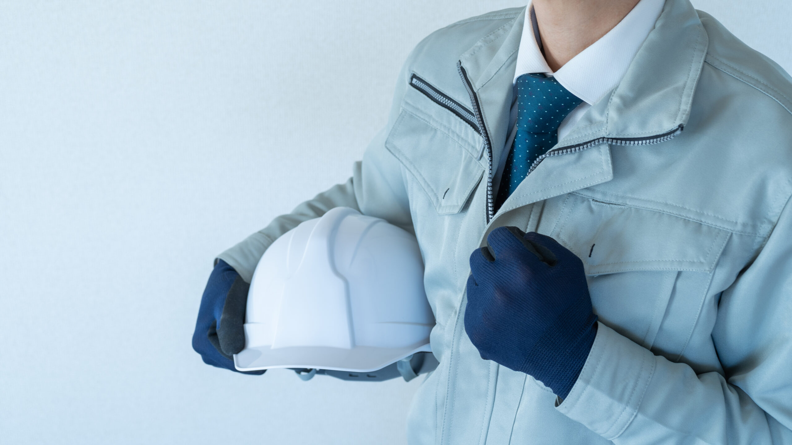 作業服にネクタイの男性。ヘルメットを抱える